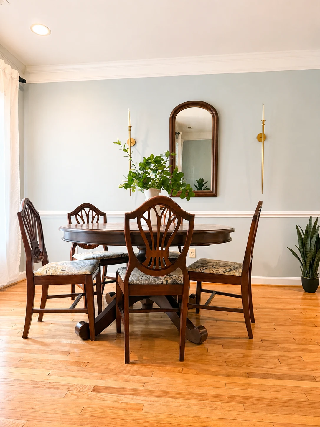 Dining room with a round wood table, carved chairs, arched mirror, and brass candle sconces