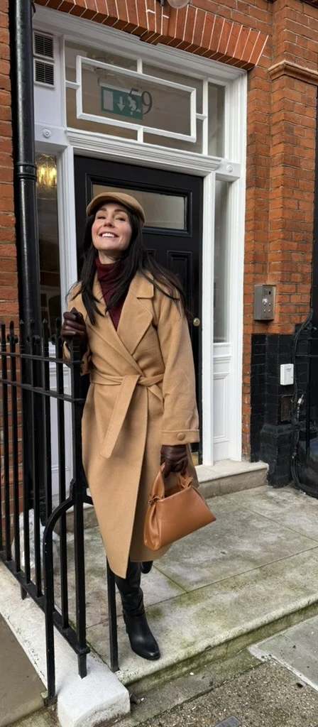 April in a camel coat and hat outside a townhouse